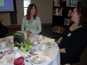 Mandy visits with a guest at our table while sitting at elegantly dressed tables adorned with pretty china dishes.